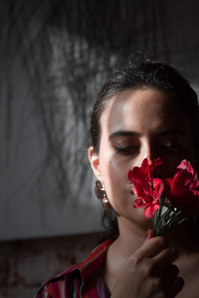 foto com modelo em primeiro plano segurando um ramo de flores vemelhas em frente ao rosto